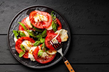 Domatesli salata, mozzarella ve koyu ahşap arka planda fesleğen. İtalyan mutfağı konsepti. Boşluğu kopyala