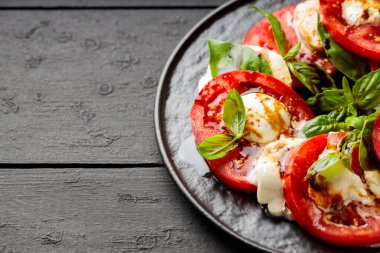Domatesli salata, mozzarella ve koyu ahşap arka planda fesleğen. İtalyan mutfağı konsepti. Boşluğu kopyala