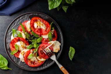 Dilimlenmiş domatesli İtalyan caprese salatası, mozzarella, fesleğen, koyu arkaplanda zeytinyağı. Uzayı kopyala Üst görünüm