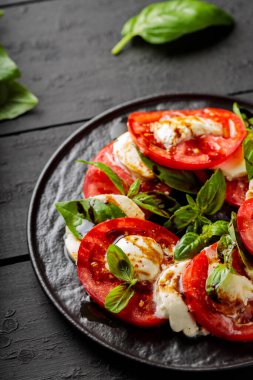 Olgun domatesli lezzetli caprese salatası, mozzarella peyniri ve koyu ahşap tahtalarda taze fesleğen yaprağı. Kapat.