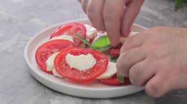 Adamın eli Caprese salatasına fesleğen yaprağı koyar. İtalyan Caprese salatası hazırlama, yakın plan.
