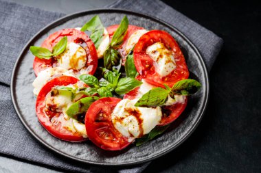 Sağlıklı klasik caprese salatası, olgun domatesler ve koyu arkaplanda taze fesleğen yapraklı mozzarella peyniri. Kapat.