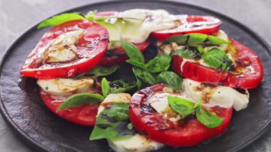 Domatesli Caprese Salatası, mozzarella ve koyu arkaplanda fesleğen yaprakları. Kapat.