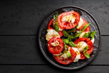 Domatesli salata, mozzarella ve koyu ahşap arka planda fesleğen. İtalyan mutfağı konsepti. Boşluğu kopyala