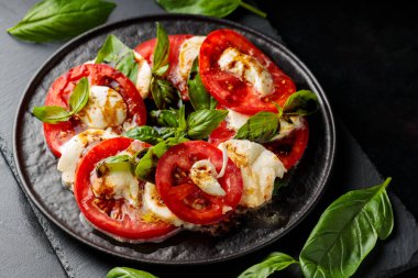 İtalyan caprese salatası, mozzarella, domates ve fesleğen. Siyah tabakta sağlıklı klasik lezzetli Caprese salatası.