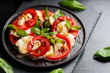İtalyan caprese salatası, mozzarella, domates ve fesleğen. Siyah tabakta sağlıklı klasik lezzetli Caprese salatası.