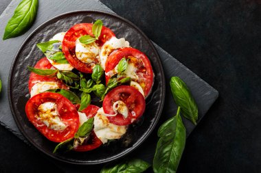 İtalyan caprese salatası, mozzarella, domates ve fesleğen. Siyah tabakta sağlıklı klasik lezzetli Caprese salatası.