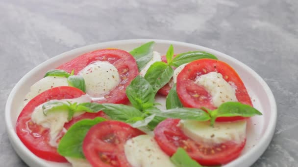 スライスされたトマト モッツァレラチーズ グレーの背景にバジルが付いたイタリアのカペラサラダ カメラの動きを傾ける — ストック動画