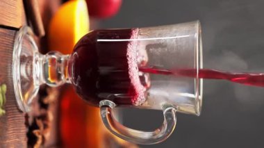 Sıcak şarap bardağa dökülür. Noel şarabı ve malzemeler ahşap masada. Dikey video