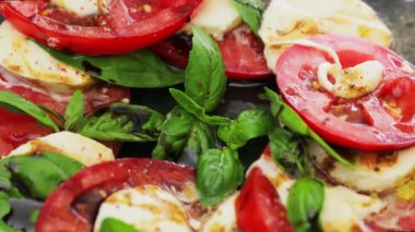 Dilimlenmiş domatesli İtalyan Caprese Salatası, koyu arkaplanda mozzarella peyniri ve fesleğen. Kapat.