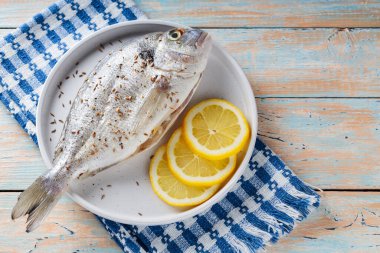 Limonlu çiğ dorado balığı ve ahşap masa üzerinde kimyon tohumları.