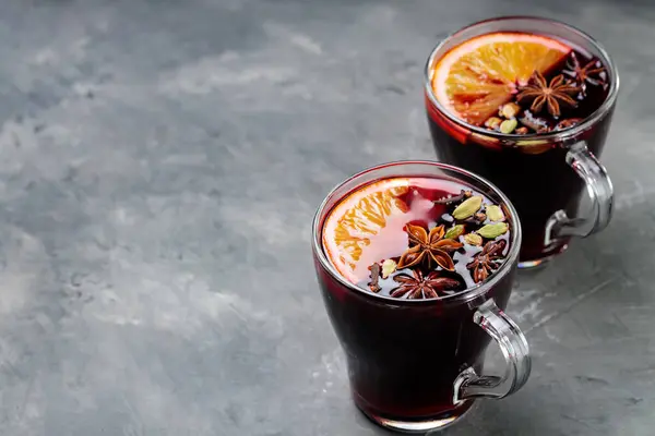 Mulled wine in transparent mugs with spices and orange fruit on concrete. Traditional autumn drink. Copy space