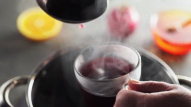 Adam şeffaf bardağa kepçeyle şarap döker, yakın çekim. Mevsimlik sıcak içecek.