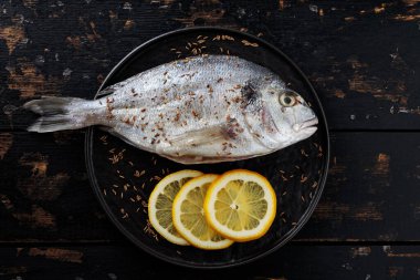 Limonlu çiğ dorado balığı ve siyah tabakta kimyon tohumları. Üst görünüm