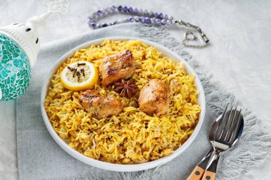 Gri arka planda çatal bıçaklı geleneksel tavuk biryani tabağı, yakın plan.