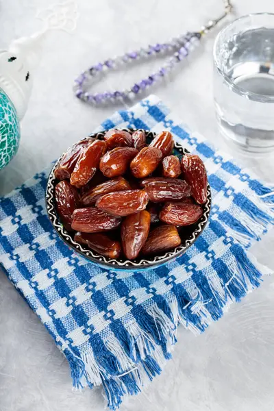 Bowl of Dates, Water and Prayer Beads on Gray Background, Islamic Religion and Ramadan Concept