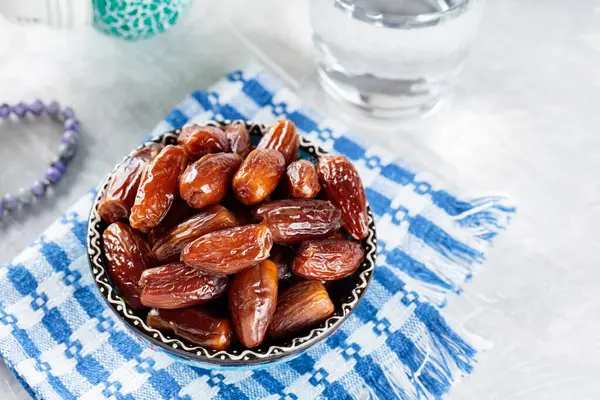 Bowl of Dates, Water and Prayer Beads on Gray Background, Islamic Religion and Ramadan Concept