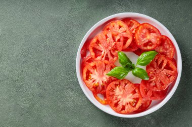 Beyaz Tabakta taze fesleğenle canlı domates dilimleri, Yeşil desenli arka plan, Üst Görünüm, Kopyala Boşluk