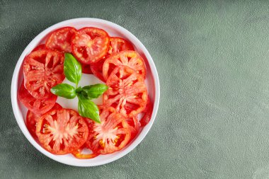 Olgun domates dilimleri ve yeşil desenli yüzeyde taze fesleğen içeren sağlıklı yaz salatası.