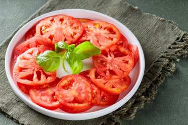 Olgun domates dilimli salata tabağı ve yeşil peçetede taze fesleğen, yakın plan.
