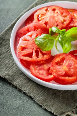 Olgun domates dilimli salata tabağı ve yeşil peçetede taze fesleğen, yakın plan.
