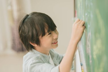 Asian boy happy smile enjoy education at school in classroom writing answer at chalkboards