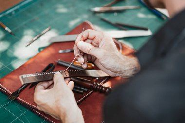 closeup hand working process leather handcraft in the leather workshop. Man holding crafting tool and working. He is sewing to make a walet. Tanner in old tannery.