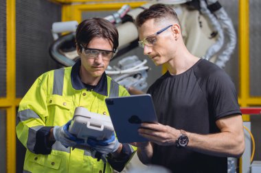 Otomatik fabrikada robot kaynak kolu üzerinde çalışan mühendis takımı. Robot uzmanları makine endüstrisi fabrikasında birlikte konuşuyorlar.