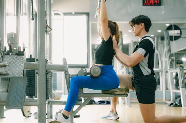 spor kadını göğüs kaslarını çalıştırıyor spor salonunda, erkek antrenörle birlikte.
