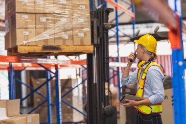 Fabrika Depo İşçisi, kargoyu nakliye alanındaki envanter kontrol ustabaşısına yüklüyor..