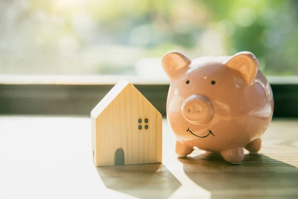 stock image smile piggy bank with home wood house model morning sunlight background