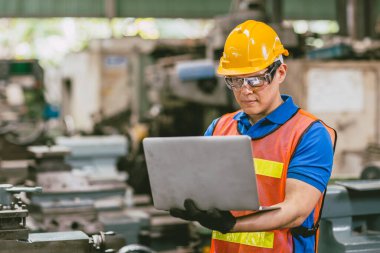 Asian male engineer worker happy using Laptop computer in heavy metal factory background. clipart