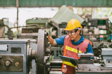 Young Asian Technician Engineer Staff Worker using Lathe CNC Milling Machine work in Heavy Metal Factory. clipart