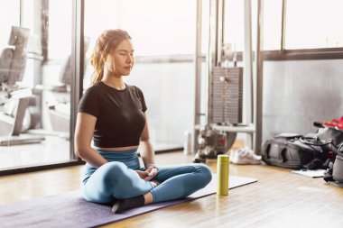 Genç Asyalı kadın yoga yapıyor meditasyon egzersizi yapıyor, dinleniyor rahat poz veriyor spor kıyafetleri giyiyor, iç mekanda meditasyon yapıyor spor kulübünün iç kısımlarını inceliyor..