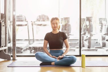 Genç Asyalı kadın yoga yapıyor meditasyon egzersizi yapıyor, dinleniyor rahat poz veriyor spor kıyafetleri giyiyor, iç mekanda meditasyon yapıyor spor kulübünün iç kısımlarını inceliyor..