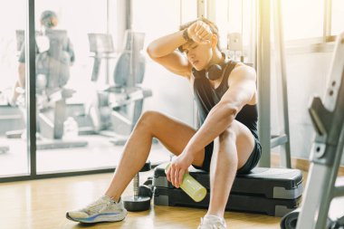 Genç adam spor kulübünde aşırı antrenman sendromundan yorgun düşüyor. Fren yapıyor, dinleniyor, terliyor, ağırlık çalıştırıyor..