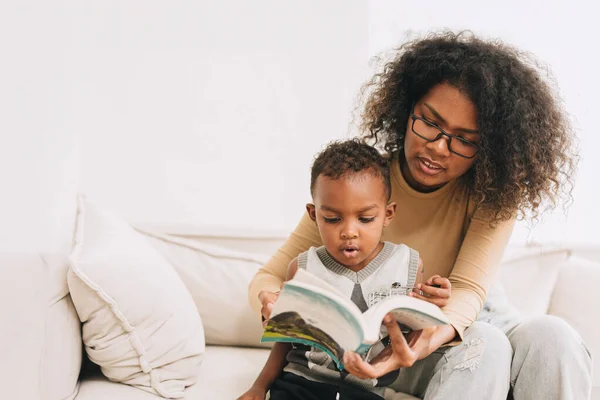 教育母亲让小男孩学习有趣的书给聪明的孩子 非洲黑人家庭看 — 图库照片