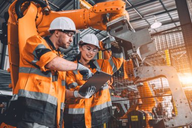 Otomasyon fabrikasında çalışan mühendis ekip servis robotu. Güvenlik kıyafeti giyen insanlar robotik kol yazılım programlama ya da otomatikleştirilmiş imalat endüstrisi teknolojisinde yer değiştirme işinde çalışıyorlar..