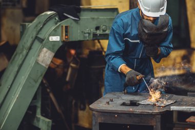 Kaynak işçisi ekibi ağır endüstri tehlikesinde ortak metal üretimi yapıyor ve göz güvenlik ekipmanlarıyla iş yeri riskini göze alıyor