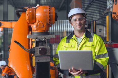 Bilgisayar kontrolü kullanan mutlu mühendis portresi robotlu kol makinesi. Otomasyon fabrikasında insan programlama robotu kaynak makinesi