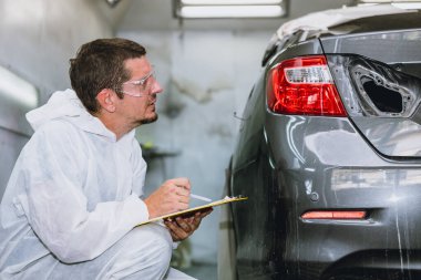 Araba boyacısı profesyonel erkek işçi oto tamirhanesindeki boya detaylarını kontrol ediyor.