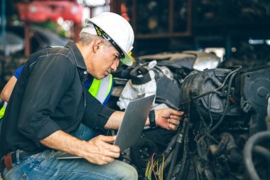 Kıdemli mühendis takımı envanter dükkanını kontrol ediyor. Eski yedek yedek parça motor teçhizatı. Garaj tamir pazarında geri dönüşüm listesi.