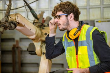 Ağır metal otomasyon fabrikasında otomatik robot kaynak makinesi programlayan akıllı genç mühendis.
