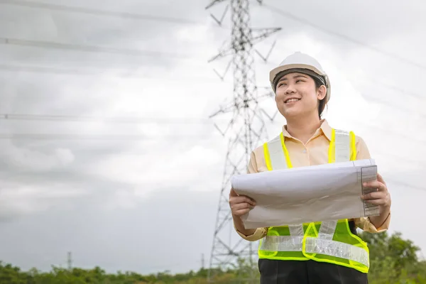 Happy engineer woman happy smiling with high voltages electricity transmission pole building project on background