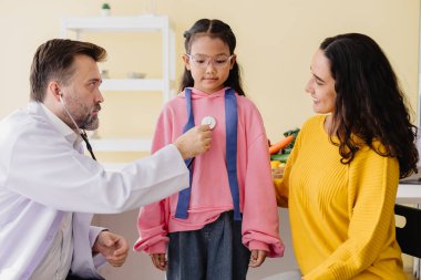Anne ve kızı sağlık kontrolü için klinikte çocuk doktoruyla görüşüyor..