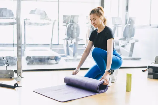 Fitness woman in sport club studio with yoga mat. Young woman roll pilates mat at a fitness training class.