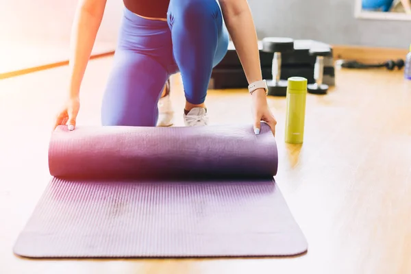 Closeup fitness woman in sport club studio with yoga mat. Young woman roll pilates mat at a fitness training class.
