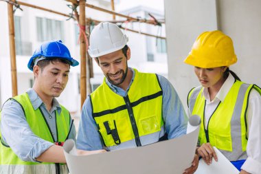 Mimar ve ustabaşıyla çalışan mutlu bir inşaat işçisi grubu kat planıyla ilgili proje planlarını konuşuyorlar.