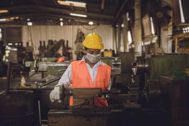 Ağır metal makinesiyle çalışan genç Asyalı kadın işçi değirmen fabrikası sanayii hijyen için kirli işyeri koruyucu yüz maskesi.