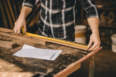 Yakından marangoz erkek el, mobilya projesi için tahta çubuğun uzunluğunu ölçmek için mezura kullanıyor.